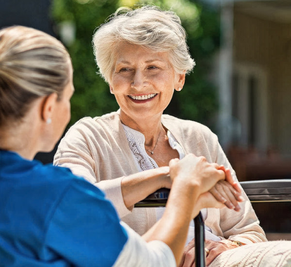 A caregiver sitting with a resident outdoors, holding her hand